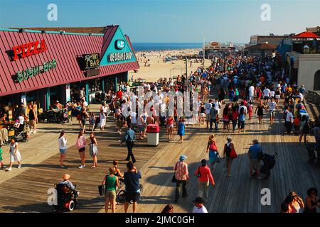 An einem sonnigen Sommerurlaubstag an der Jersey Shore spazieren die Leute entlang des Point Pleasant Boardwalk und betreten die Bars und Restaurants Stockfoto