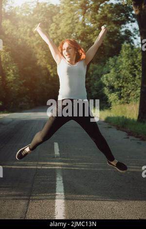 Sportliche junge Rothaarige Frau, die vor Freude hüpft Stockfoto