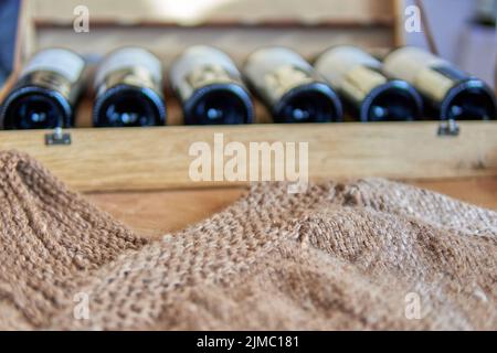 Holzkiste aus Rotweinflaschen mit einem handgefertigten braunen Poncho auf der Vorderseite. Besuch einer Weinkellerei in mendoza, argentinien. Selektiver Fokus Stockfoto