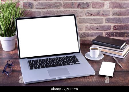 Laptop-Notebook mit leerem Bildschirm und Tasse Kaffee und Notizblock Stift und Bücher und Smartphone auf Holz Stockfoto