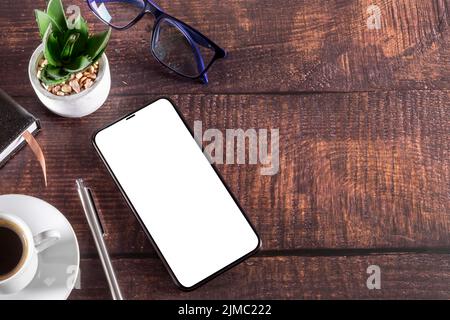 Arbeitstisch mit Smartphone Notizblock Kaffeetasse Stift Gläser Pflanze auf Holz Stockfoto