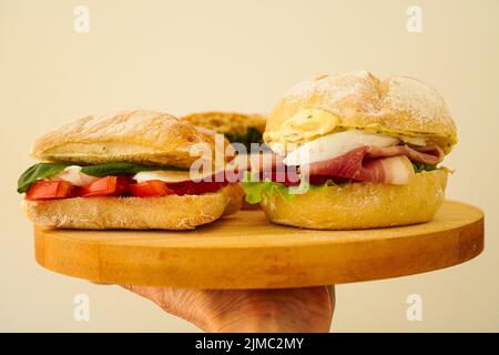 Sandwich Panini und Frauenhand mit italienischen Sandwiches Panini auf Holzbrett Stockfoto