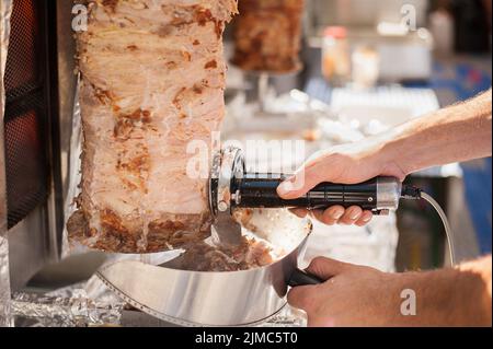 Die Hände der Köchin, die mit elektrischen Messer der Döner Kebab Schneiden. Stockfoto