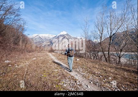 Mann Wanderer, der auf dem Weg über das Flussufer in Richtung Berge geht. Stockfoto