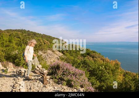 Weibliche Wanderer sammelt wilde Salbei auf einer Klippe mit Blick auf das Meer. Stockfoto