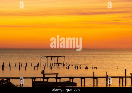 Der Himmel leuchtet in Orange-Tönen, als die Sonne über der Mobile Bay untergeht, wie sie von Fairhope, Alabama, aus gesehen wird, in einem zusammengesetzten Bild. Stockfoto