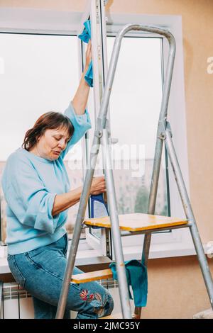 Glücklich Schüchtern Reifen Frau Reinigung Fenster. Kaukasische Frau Im Mittleren Alter. Ältere Frau Reinigung Apartment. Konzept Für Aktive Senioren. Hausfrau. Konzept Von Stockfoto