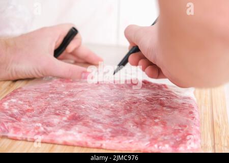 Ein Mann signiert mit einem Marker das Produktionsdatum und ein Gramm gehacktes Schweinefleisch und Rindfleisch, das in Säcken zur Lagerung im Gefrierschrank ausgelegt wird. Produktkennzeichnung. Stockfoto