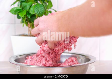 Ein Mann mischt Hackfleisch in einer Schüssel mit seinen Händen. Zubereitung von Hackfleisch und Schweinefleisch für Koteletts, Fleischbällchen, Koteletts. Stockfoto