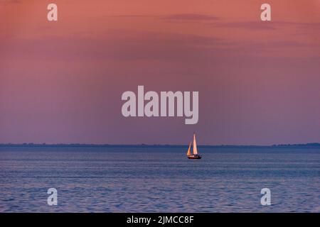 Bei Sonnenuntergang schwimmt ein Segelboot auf der Mobile Bay. Stockfoto