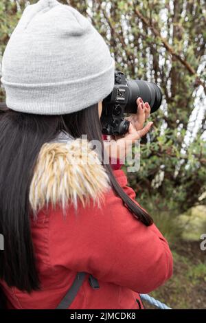 Arbeiten Aufnahme von Fotos junge Frau in Wollmütze mit langen Haaren hält professionelle Kamera, Hobby-Tool, Lifestyle Stockfoto