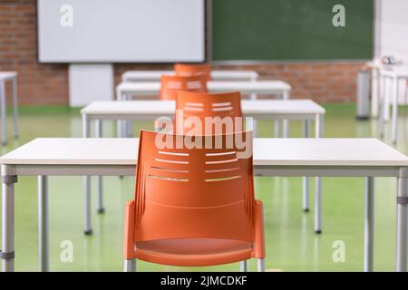 Dekoration des Innenraums eines Klassenzimmers in einer Schule mit Schreibtischen, farbigen Stühlen und Tafel. Lehrplatz mit bequemen Möbeln Stockfoto