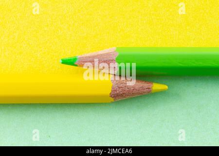 Farbstifte auf gelbem und grünem Papier, horizontal angeordnet. Stockfoto
