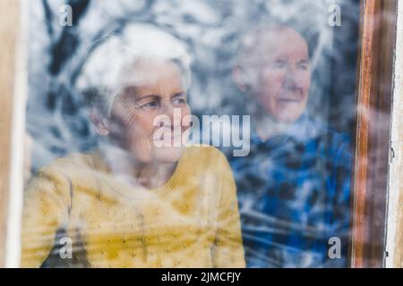 Liebevolles kaukasisches älteres Ehepaar zu Hause, das durch das Fenster schaute und den Schnee während der Wintersaison bewunderte. Hochwertige Fotos Stockfoto