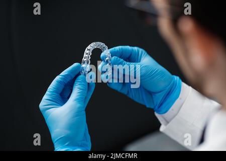 Unsichtbare Kieferorthopädie kosmetische Ausrichter in den Händen des Arztes tragen sterile Handschuhe isoliert auf schwarzem Hintergrund, Zahnausrichter, Kunststoff-Zahnspangen. Mod Stockfoto