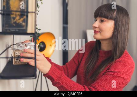 Attraktive reife Frau mit langen, geraden braunen Haaren, die Gegenstände neu anordnen und das Wohnzimmer dekorieren. Hochwertige Fotos Stockfoto
