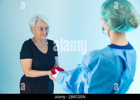 Eine glückliche ältere europäische Frau und ein Chirurg Arzt in einer medizinischen Schutzkleidung mit rotem künstlichem Herzen. Hochwertige Fotos Stockfoto