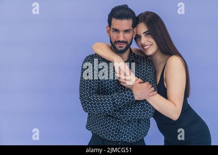 Die junge Brünette umarmte ihren Mann lächelnd und lehnte sich auf seine Schulter und wickelte ihre Hand um ihn. Beide blicken in die Kamera. Glückliches Paar. Studioaufnahme. Hochwertige Fotos Stockfoto
