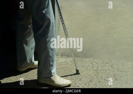 Gehstock. Ein Mann mit einer Beinverletzung. Behindert mit einem Gerät zur Unterstützung beim Gehen eines alten Mannes in weißen Schuhen. Stockfoto
