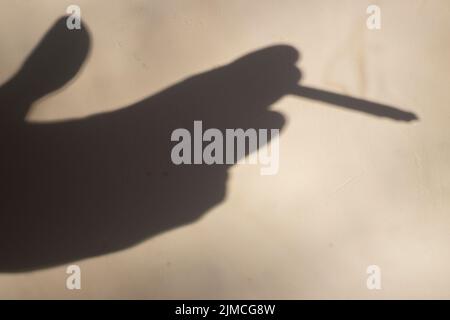 Schatten einer Zigarette in der Hand. Rauchen ist gesundheitsschädlich. Einsamkeit und Rauchen. Die Hand hält eine Zigarette. Stockfoto