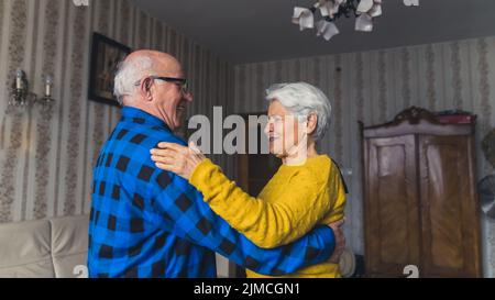 Fröhliches aktives altes Paar, das im Wohnzimmer tanzt und lacht und Spaß zu Hause hat. Hochwertige Fotos Stockfoto