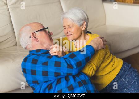 Entspanntes, wunderschönes, liebevolles, umarmtes Senioren-Familienpaar, das sich ansah und lächelte, während es auf dem Boden neben der Couch im Wohnzimmer zu Hause saß. Hochwertige Fotos Stockfoto