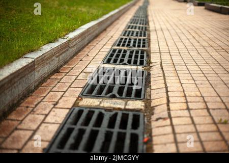 Sturmabfluss für die Wasserableitung. Details der städtischen Kommunikation. Luken des Kanals. Rost auf der Straße. Abfluss für Regenwasser. Stockfoto