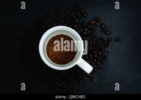 Draufsicht auf Instant-Kaffee in der Tasse auf dunklem Hintergrund mit Bohnen Stockfoto