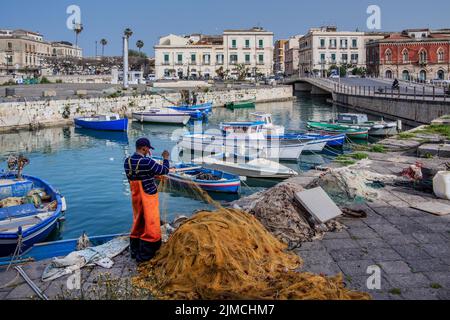 Fischer flicken Netze am Fischereihafen mit Booten vor der Altstadt, Syrakus, Ostküste, Sizilien, Italien Stockfoto