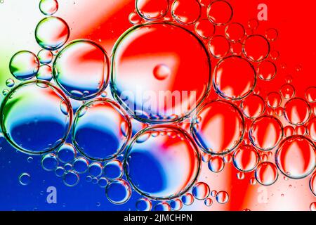 Abstrakter Hintergrund von Ölblasen auf Wasseroberfläche rot weiß blau Palette. Stockfoto