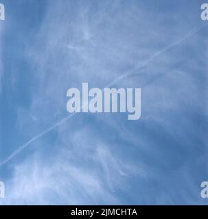 Dampfspur vom Flugzeug gegen Wolken am blauen Himmel Stockfoto