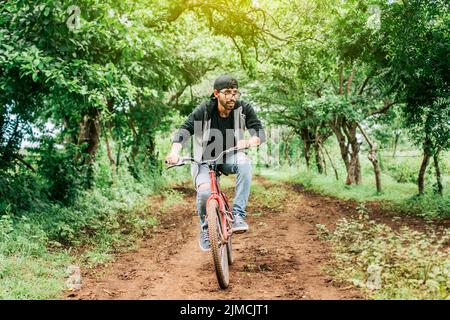 Teenager, der auf dem Land ein Fahrrad fährt, Porträt eines Mannes in Cap, der auf einer Landstraße ein Fahrrad fährt, Person, die auf dem Land ein Fahrrad fährt Stockfoto