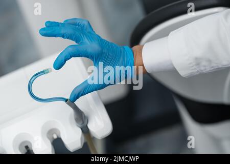 Speichelauswerfer und eine Hand in einem Einweghandschuh symbolisieren die Liebe in der Zahnmedizin. Hand in einen blauen Handschuh mit blauem Speichelauswerfer. Herzsymbol. Stockfoto