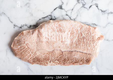 Blick von oben auf das traditionelle japanische, ungekochte wagyu-Rindfleisch der Präfektur kobe, das während der Zubereitung auf einem Marmortisch im hellen Raum aufgestellt wurde Stockfoto