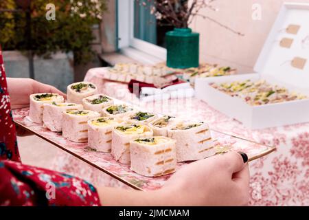 Eine nicht erkennbare Frau, die während des Banketts auf der Terrasse des Gebäudes am Sommertag leckere Tortilla-Rollen auf dem Tisch serviert Stockfoto