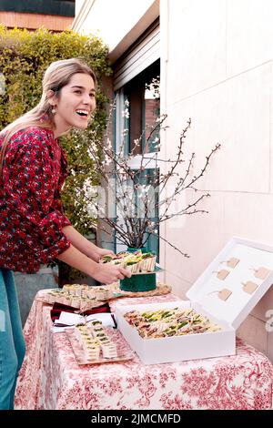 Seitenansicht einer positiven, fröhlichen Frau, die am Sommertag auf der Terrasse des Gebäudes leckere Tortilla-Rollen auf dem Tisch serviert Stockfoto