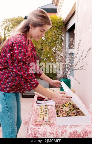 Seitenansicht einer positiven Frau, die während des Banketts auf der Terrasse des Gebäudes am Sommertag leckere Tortilla-Rollen auf dem Tisch serviert Stockfoto