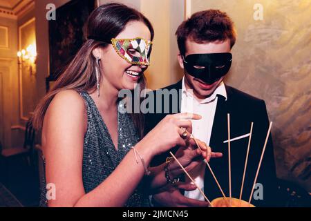 Content Freunde in Maskerade Masken essen leckere Melonenbälle, während festliche Veranstaltung zusammen in hellen modernen Restaurant feiern Stockfoto