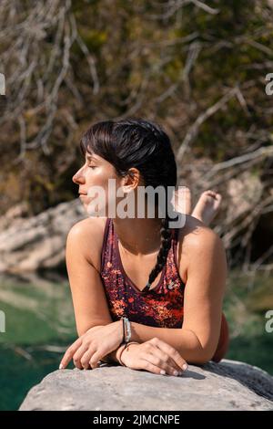 Porträt einer Frau, die sich auf einem Felsen neben dem Fluss entspannt, während sie die Augen schließt Stockfoto