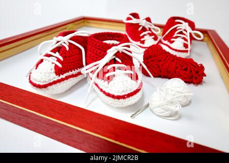 Babyschuhe oder Häkelschuhe in rot und weiß isoliert auf weißem Hintergrund Stockfoto