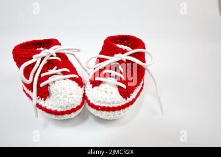 Babyschuhe oder Häkelschuhe in rot und weiß isoliert auf weißem Hintergrund Stockfoto