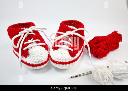 Babyschuhe oder Häkelschuhe in rot und weiß isoliert auf weißem Hintergrund Stockfoto