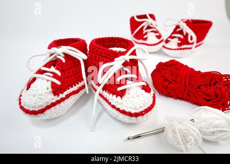 Babyschuhe oder Häkelschuhe in rot und weiß isoliert auf weißem Hintergrund Stockfoto