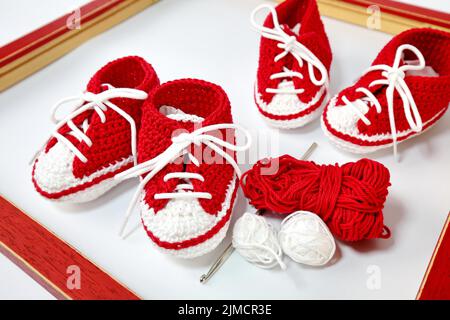 Babyschuhe oder Häkelschuhe in rot und weiß isoliert auf weißem Hintergrund Stockfoto