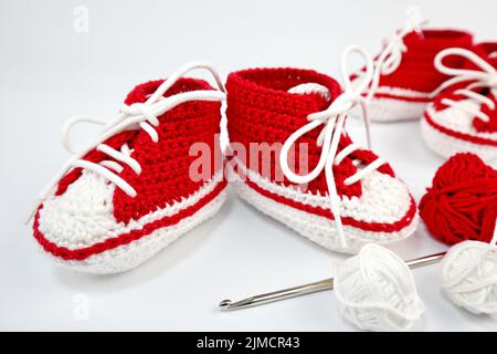 Babyschuhe oder Häkelschuhe in rot und weiß isoliert auf weißem Hintergrund Stockfoto