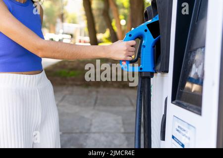 Seitenansicht der zugeschnittenen, nicht erkennbaren weiblichen Fahrerin, die an der Tankstelle in der Stadt eine Düse zum Betanken des Autos nimmt, während sie wegschaut Stockfoto