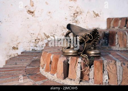 Bronzefarbene Stiefel mit Schnürsenkeln, die an sonnigen Tagen auf der Straße auf schäbigen Ziegeltreppen platziert sind Stockfoto