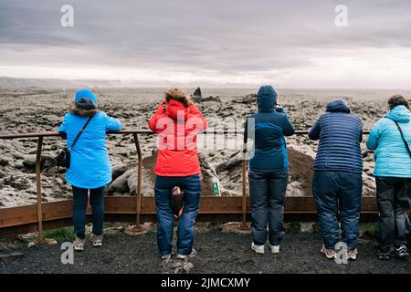 Rückansicht von unkenntlichen männlichen und weiblichen Reisenden in warmen Jacken, die am Aussichtspunkt stehen und die malerische Landschaft der Eldhraun Lavafelddecke bewundern Stockfoto