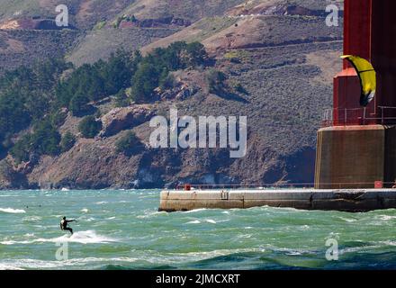 Kitesurfer, die auf den besten Whitecaps unter der Golden Gate Bridge reiten, stehen vor der Kulisse der Marin Headlands Stockfoto