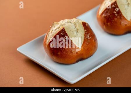 Von oben frische salzige Brezelbrötchen auf den Teller auf braunem Hintergrund gelegt Stockfoto